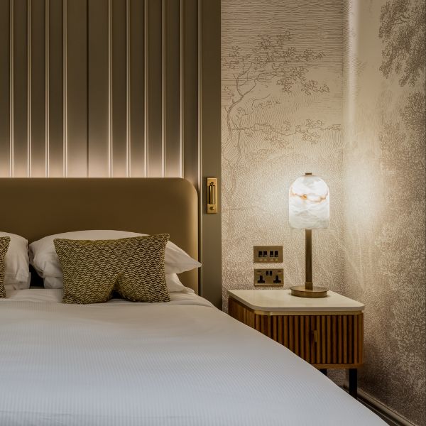 Hotel bedroom lighting trends 2026 muted hotel bedroom with panelled headboard and alabaster table lamp